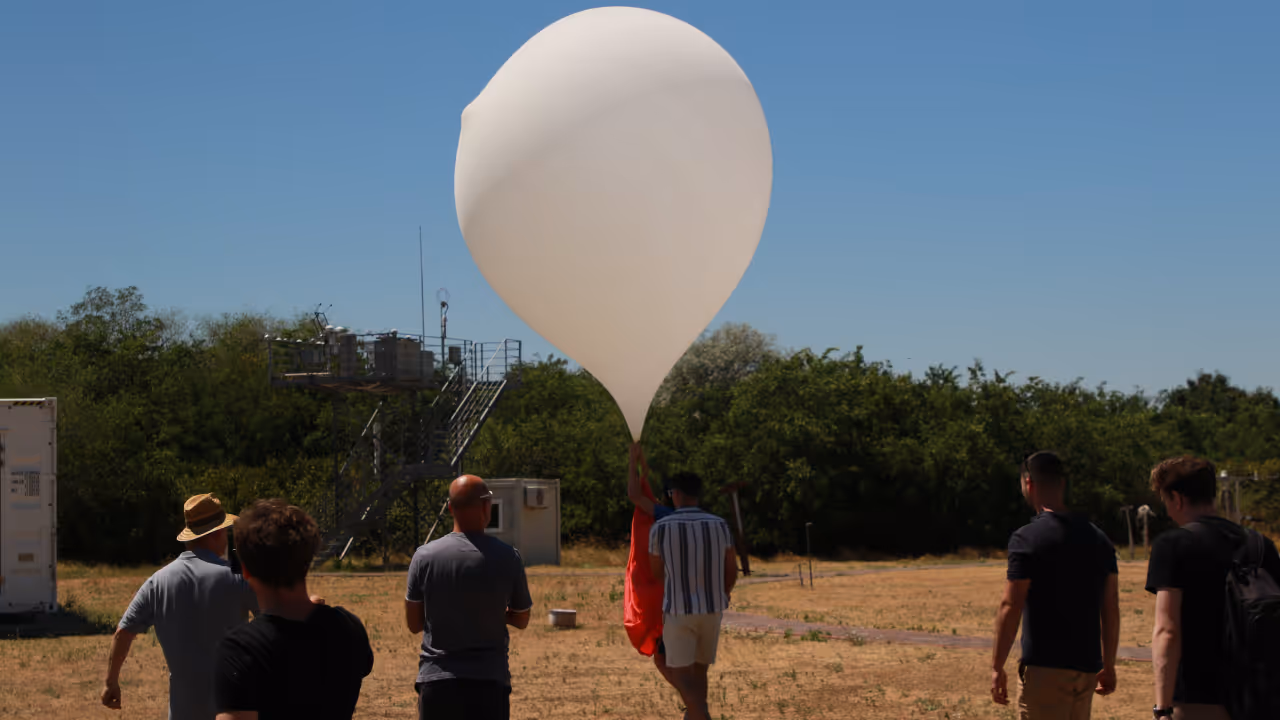 A group of people outdoors preparing to launch a large white weather balloon on a sunny day.