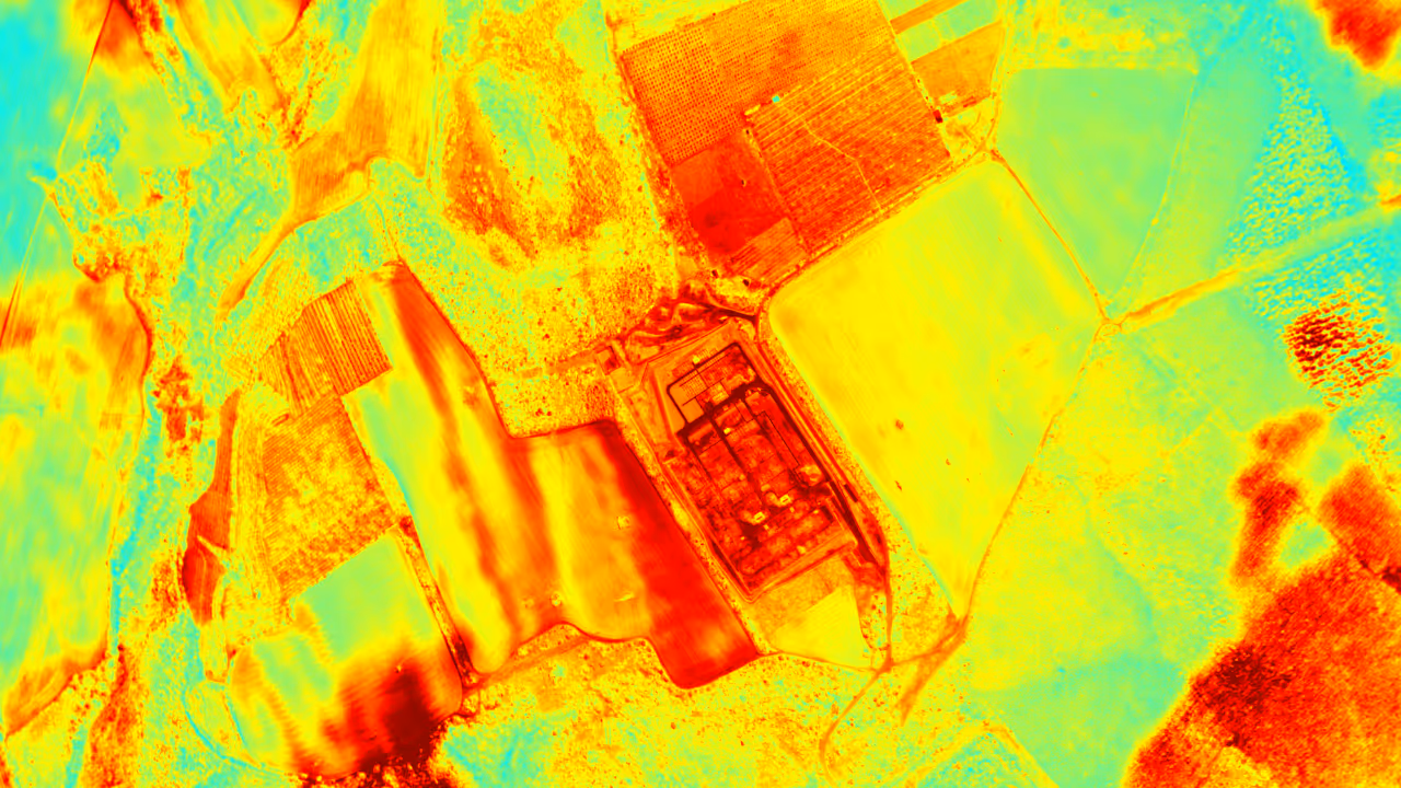 Thermal or infrared aerial image showing agricultural fields and a central facility with varying heat signatures.
